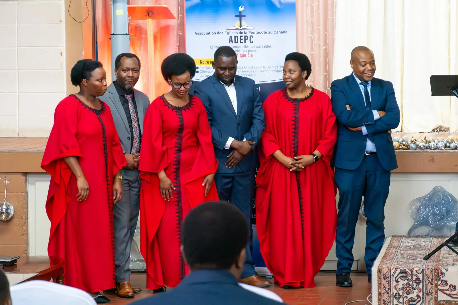 Women in matching red dresses and men in suits stand together in front of an ADEPC banner.