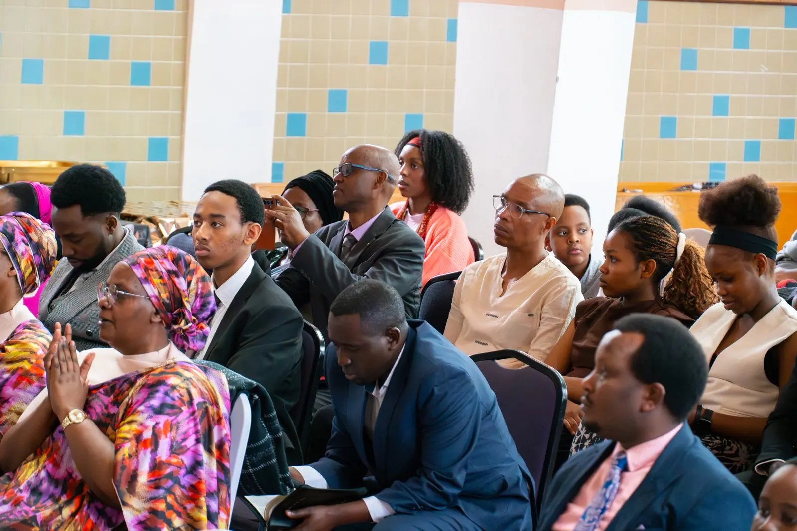 Members of the congregation seated together; a woman in a colourful dress claps her hands.
