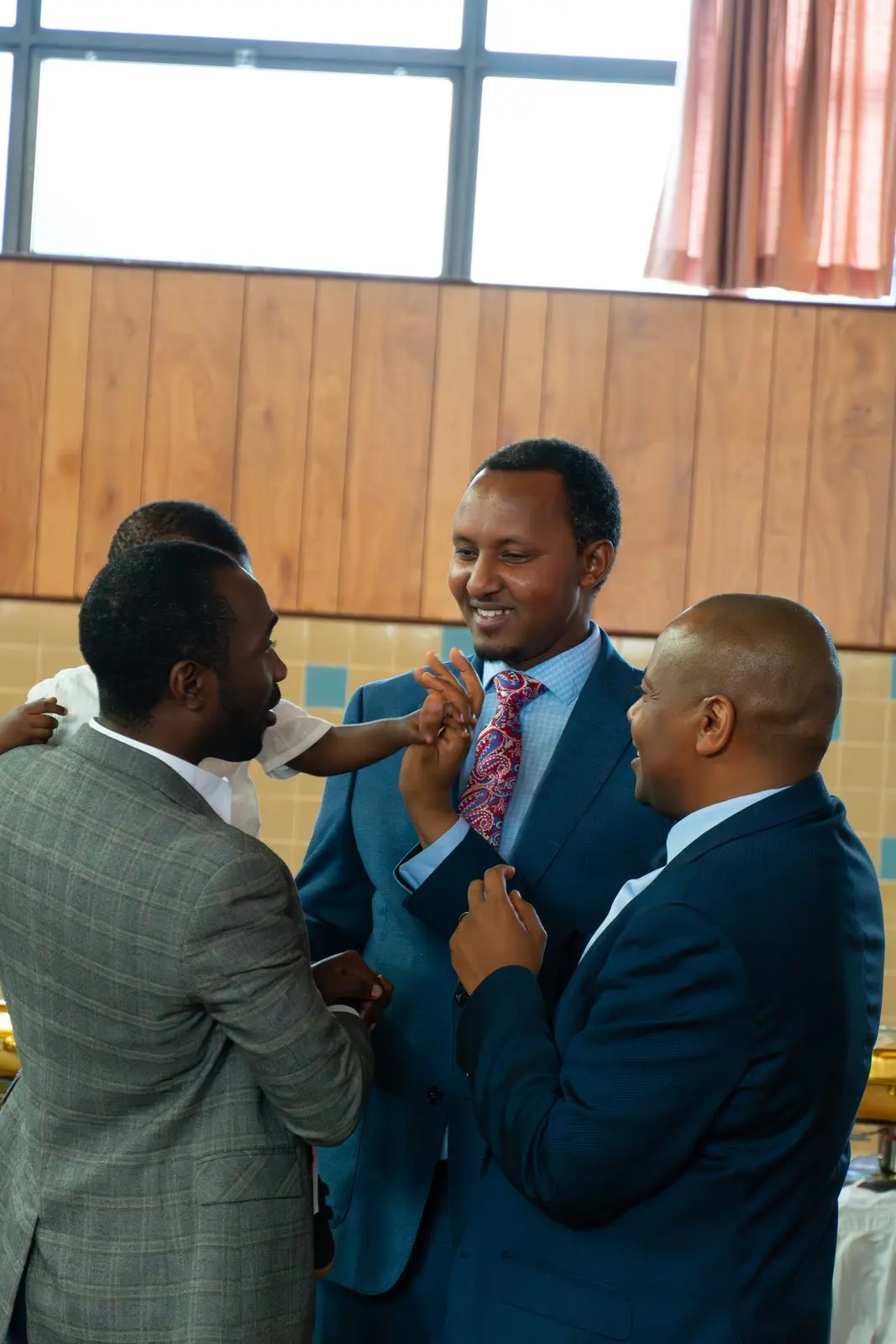Men in suits greet one another warmly in the hall.