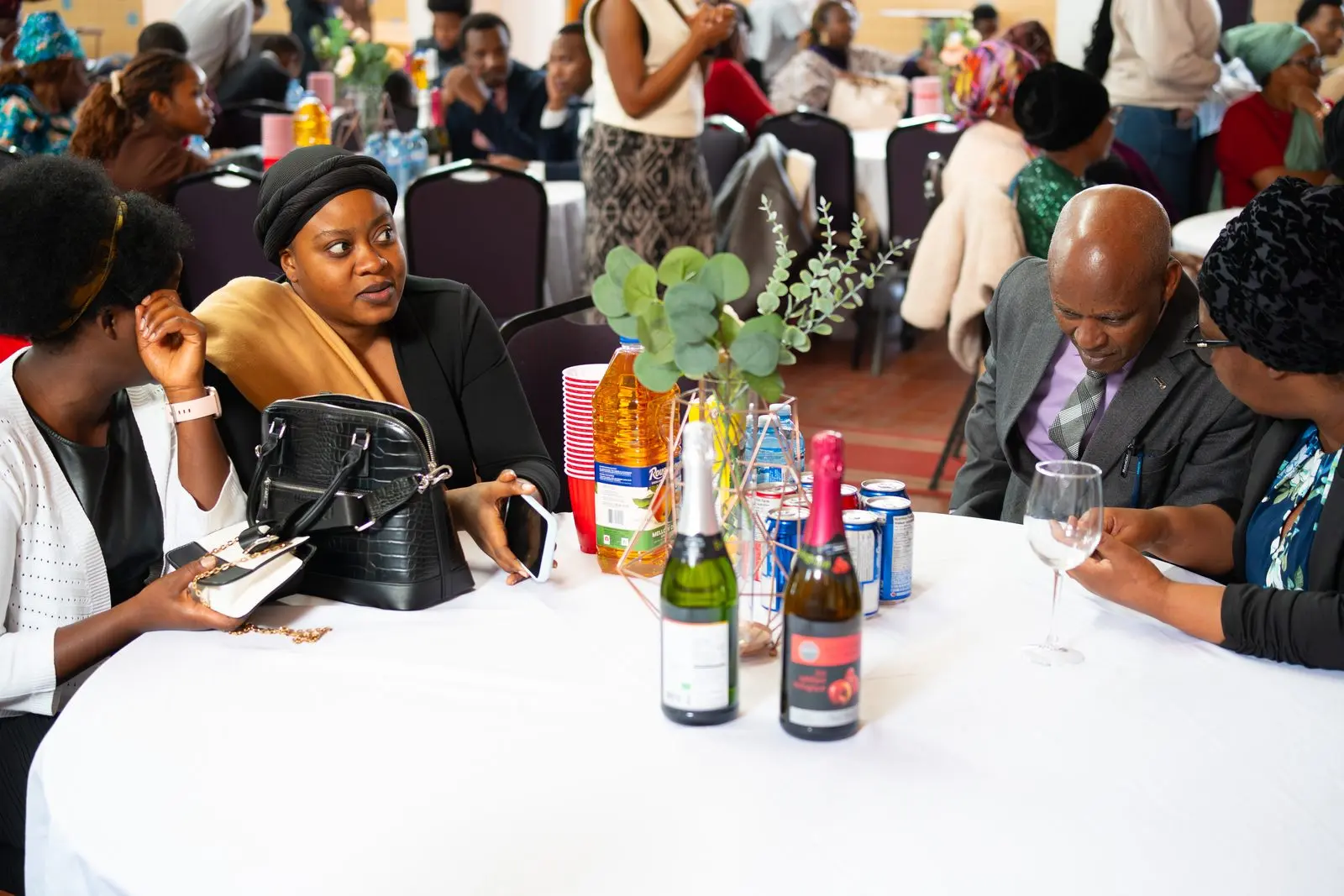 Guests talk around a round table with a white tablecloth during a celebration meal.