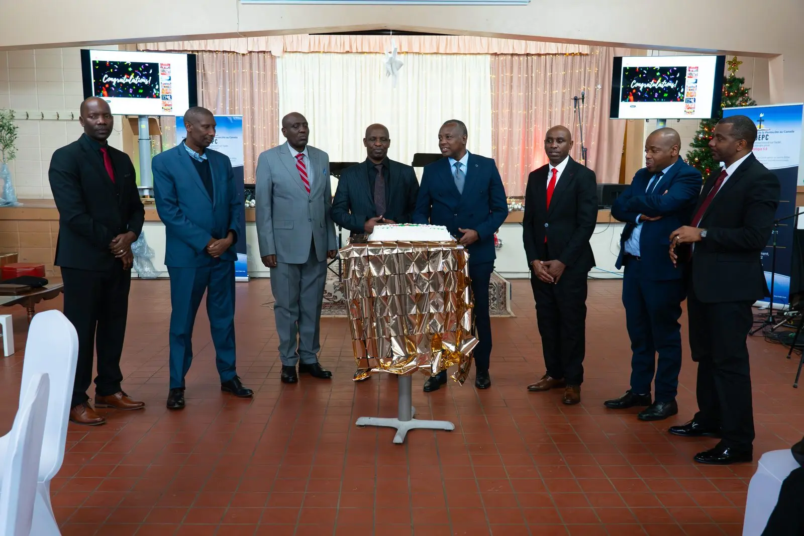 Church leaders in suits stand in a line around a decorated celebration cake.