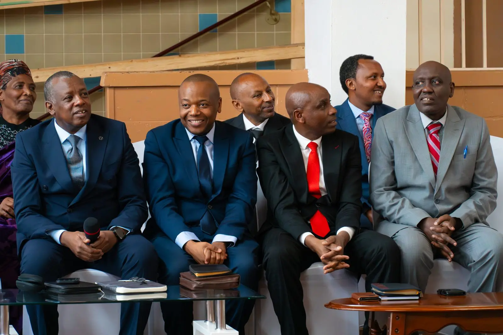 Church leaders in suits seated in the front row, smiling, their Bibles on the table before them.