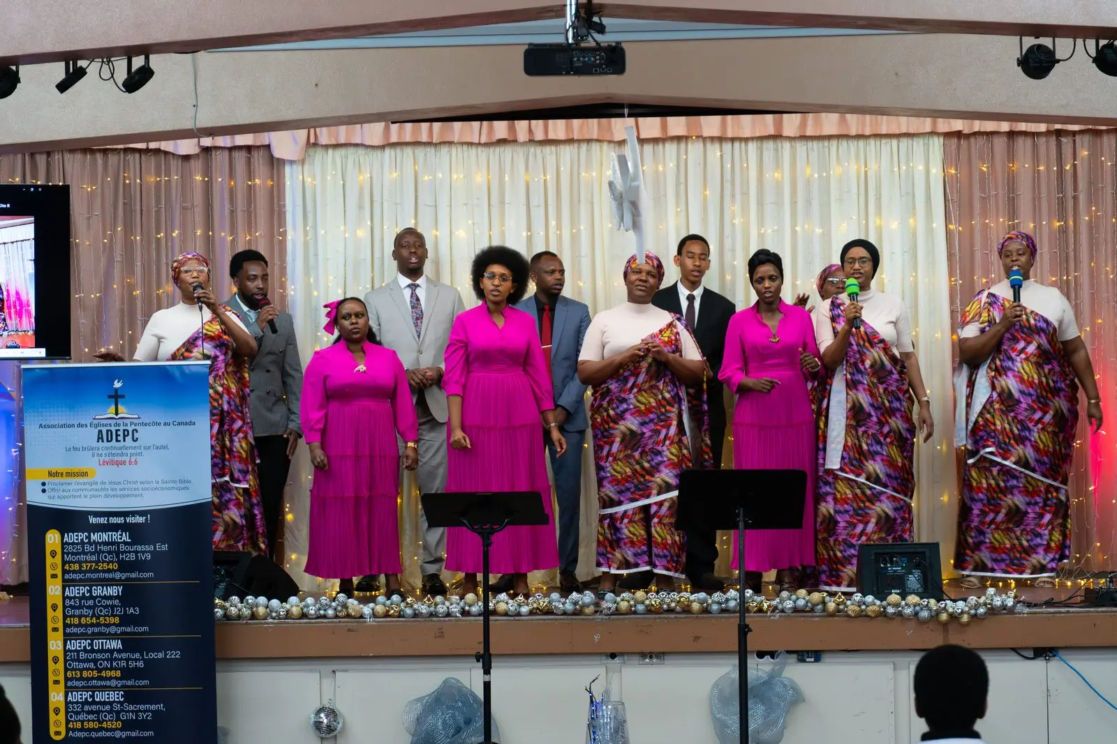 The Ottawa choir, in pink and patterned dresses, sings on stage beside the ADEPC banner.
